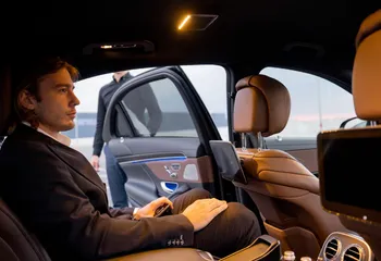 Passager en costume installé à l’arrière d’une berline haut de gamme, porte ouverte.