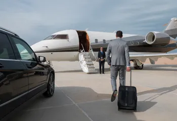 Chauffeur en costume accompagnant un voyageur vers un jet privé à l’aéroport de Nice, près d’une berline noire.