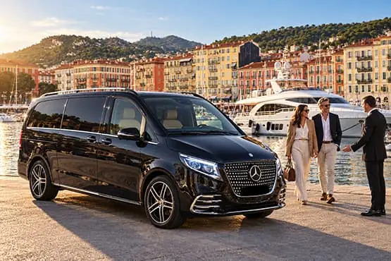 Un van noir de chauffeur privé près du port de Nice, avec des voyageurs et des bateaux en arrière-plan.