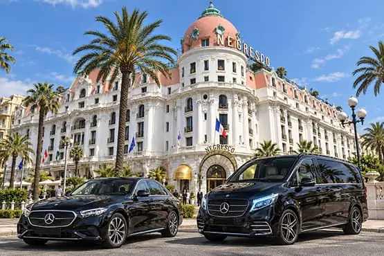 Berline et van noirs stationnés devant un hôtel bordé de palmiers à Nice.